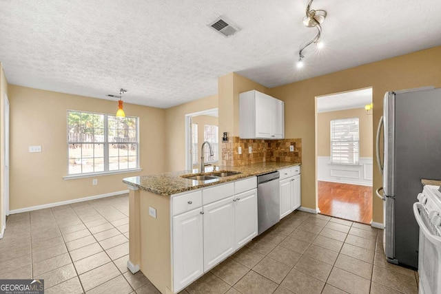 kitchen featuring light tile patterned flooring, stainless steel appliances, a peninsula, a sink, and visible vents