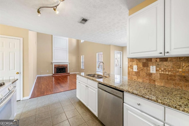 kitchen with light tile patterned flooring, a sink, visible vents, stainless steel dishwasher, and a brick fireplace