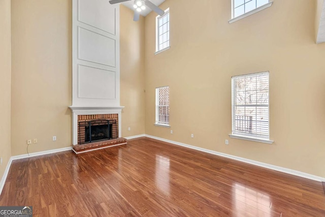 unfurnished living room with baseboards, a fireplace, a ceiling fan, and wood finished floors