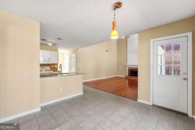 kitchen with visible vents, a brick fireplace, white cabinetry, a sink, and white appliances