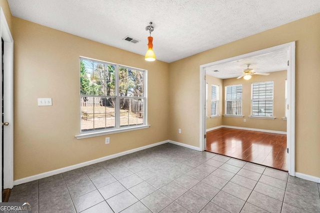 tiled empty room featuring a textured ceiling, ceiling fan, visible vents, and baseboards