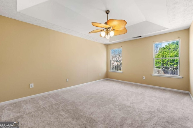 spare room with a tray ceiling, baseboards, ceiling fan, and carpet