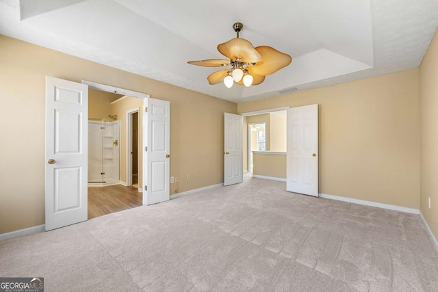 unfurnished bedroom with carpet floors, a raised ceiling, a ceiling fan, and baseboards