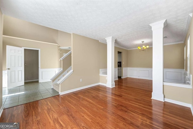 empty room with stairs, a textured ceiling, wood finished floors, and decorative columns