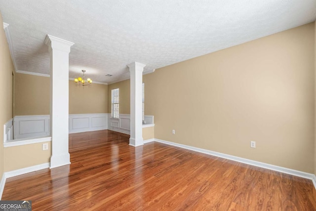 unfurnished living room with a chandelier, a textured ceiling, ornate columns, and wood finished floors