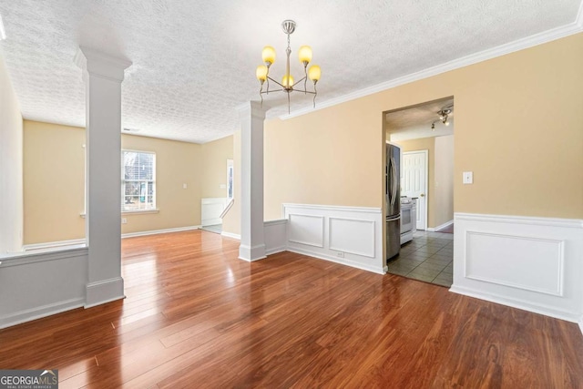 empty room with decorative columns, a textured ceiling, ornamental molding, and wood finished floors