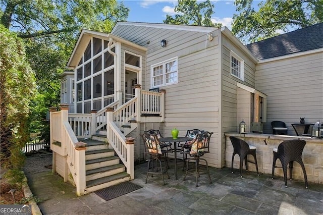 back of house with a sunroom, outdoor dry bar, roof with shingles, stairs, and a patio area