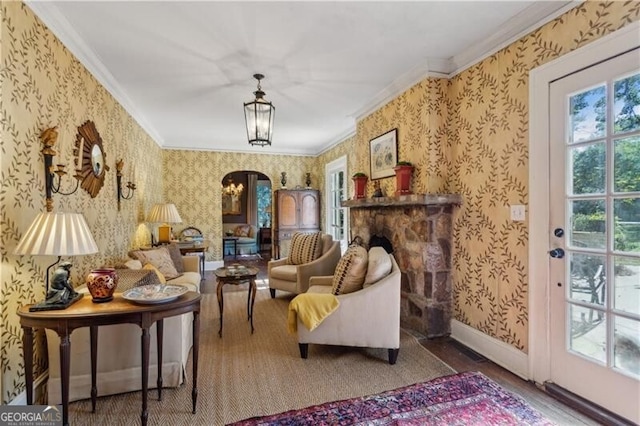 sitting room with wallpapered walls, baseboards, arched walkways, and crown molding