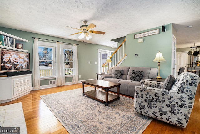 living room with stairs, a ceiling fan, a textured ceiling, and wood finished floors