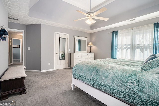 carpeted bedroom with a ceiling fan, a tray ceiling, visible vents, and baseboards