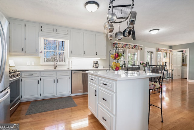 kitchen featuring a breakfast bar, stainless steel appliances, light countertops, light wood-type flooring, and a sink