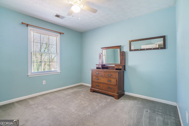 unfurnished bedroom featuring a textured ceiling, ceiling fan, carpet floors, visible vents, and baseboards