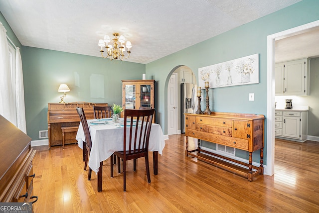 dining area featuring arched walkways, a notable chandelier, visible vents, light wood-type flooring, and baseboards