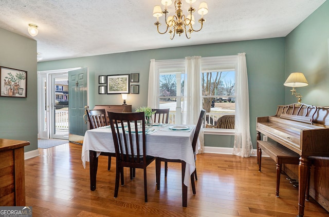 dining area with a chandelier, hardwood / wood-style floors, a textured ceiling, and baseboards