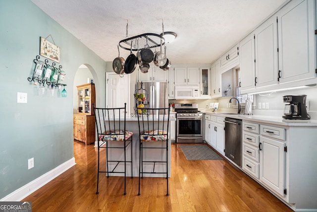 kitchen with a sink, appliances with stainless steel finishes, white cabinets, and wood finished floors