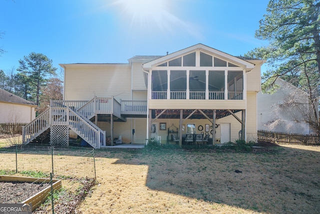 back of house featuring a yard, a vegetable garden, a sunroom, fence, and stairs