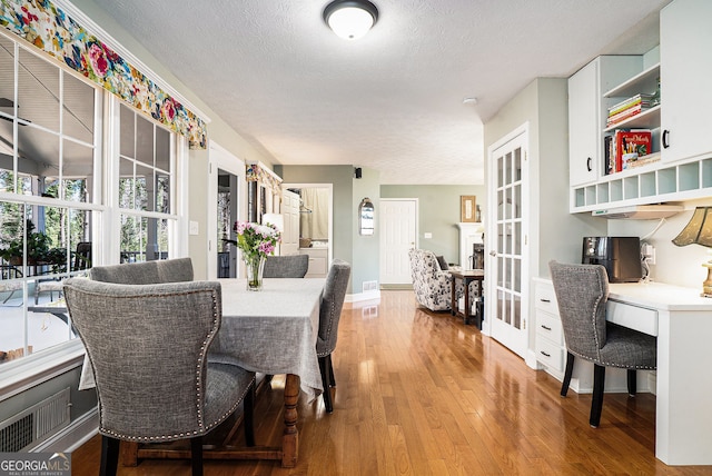 dining room with french doors, built in study area, a textured ceiling, and hardwood / wood-style floors