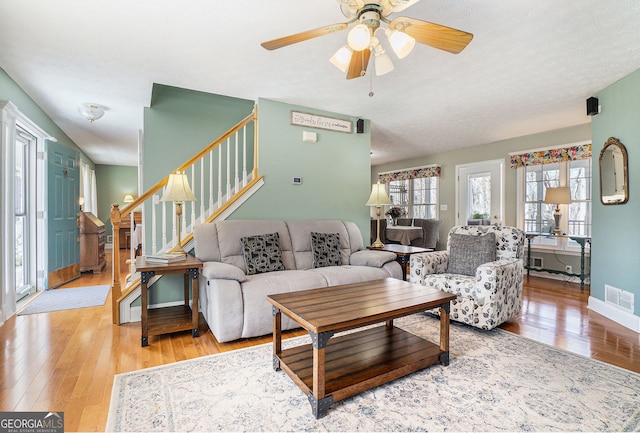 living room featuring visible vents, ceiling fan, wood finished floors, baseboards, and stairs