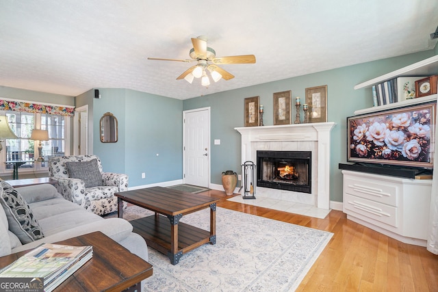 living area with a ceiling fan, baseboards, a fireplace, and light wood finished floors