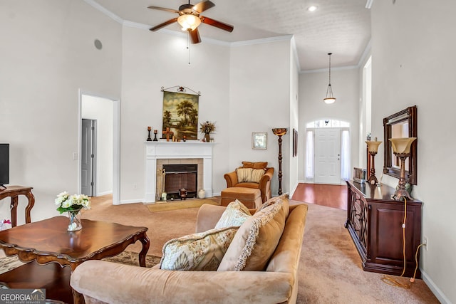 living area with baseboards, a tiled fireplace, light colored carpet, ornamental molding, and a high ceiling