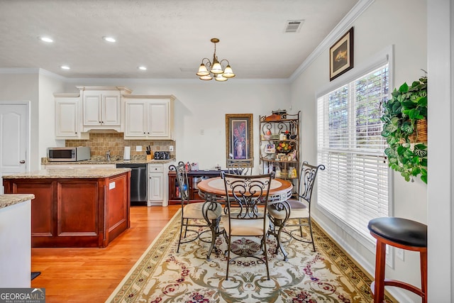 dining room with a notable chandelier, light wood finished floors, visible vents, and crown molding