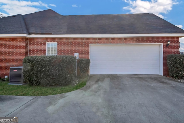 view of side of home featuring driveway, central AC unit, roof with shingles, an attached garage, and brick siding