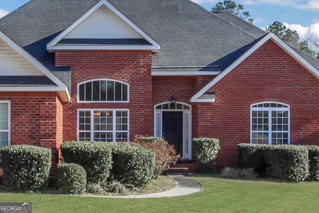 view of front of home featuring a shingled roof, a front yard, and brick siding