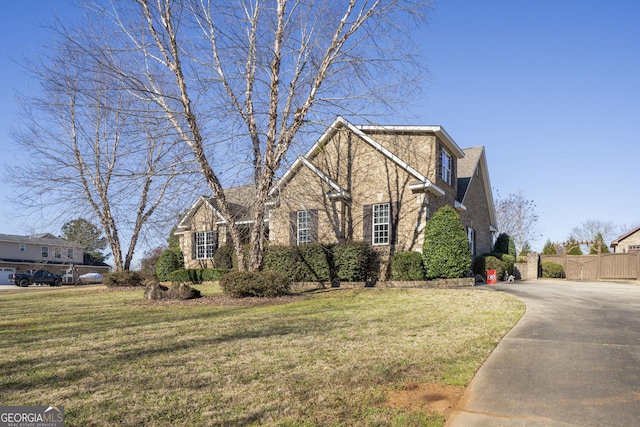 view of front of home featuring a front yard, brick siding, fence, and driveway