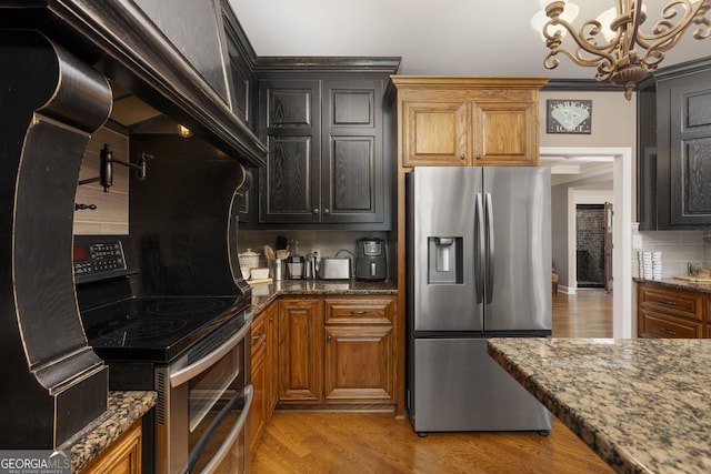 kitchen featuring brown cabinets, tasteful backsplash, appliances with stainless steel finishes, light wood-style floors, and dark stone counters