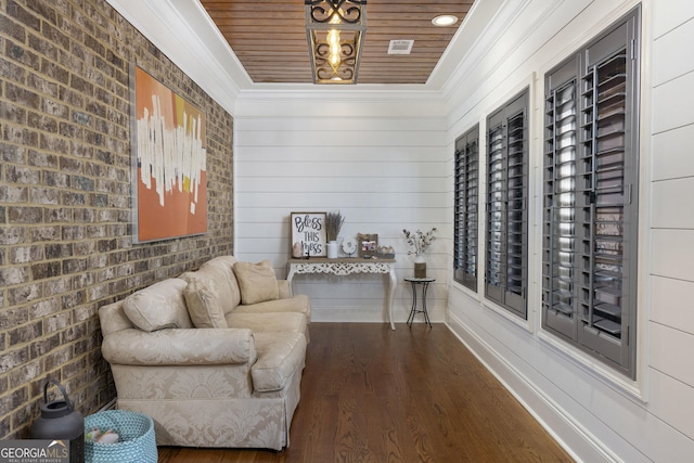 living area featuring ornamental molding, baseboards, brick wall, and wood finished floors