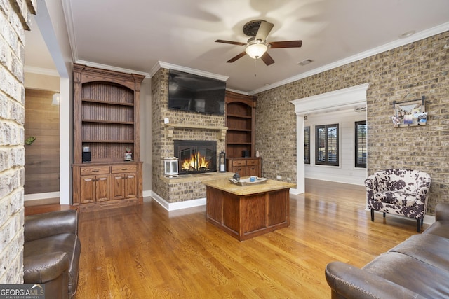 living room featuring visible vents, a ceiling fan, ornamental molding, wood finished floors, and a fireplace