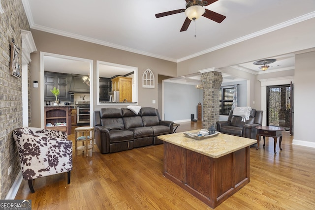 living area with decorative columns, light wood-style floors, ornamental molding, a brick fireplace, and ceiling fan