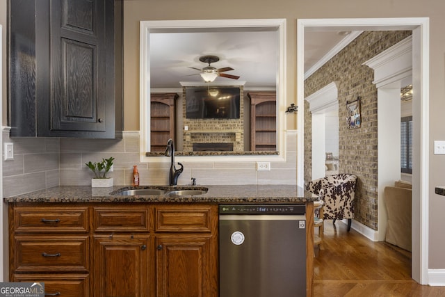 kitchen featuring stainless steel dishwasher, dark stone countertops, a sink, and crown molding