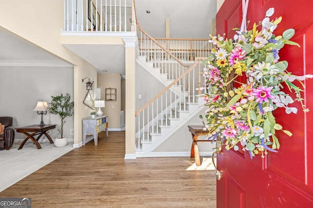 foyer with wood finished floors, a towering ceiling, baseboards, stairway, and crown molding