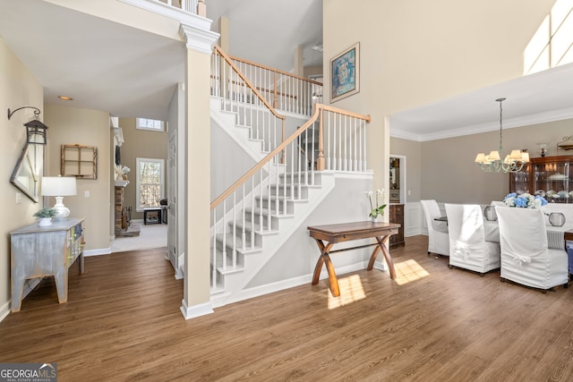 stairs with a notable chandelier, a high ceiling, wood finished floors, baseboards, and crown molding