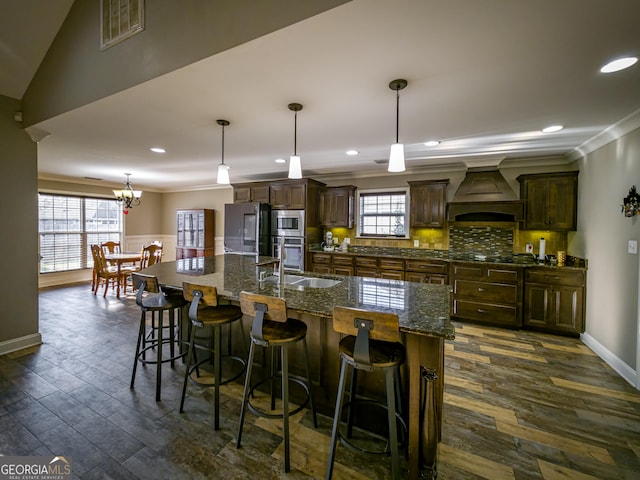 kitchen featuring refrigerator, custom exhaust hood, visible vents, ornamental molding, and a large island with sink