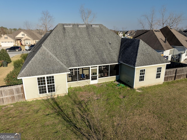 rear view of house featuring a shingled roof, a lawn, a sunroom, a residential view, and fence