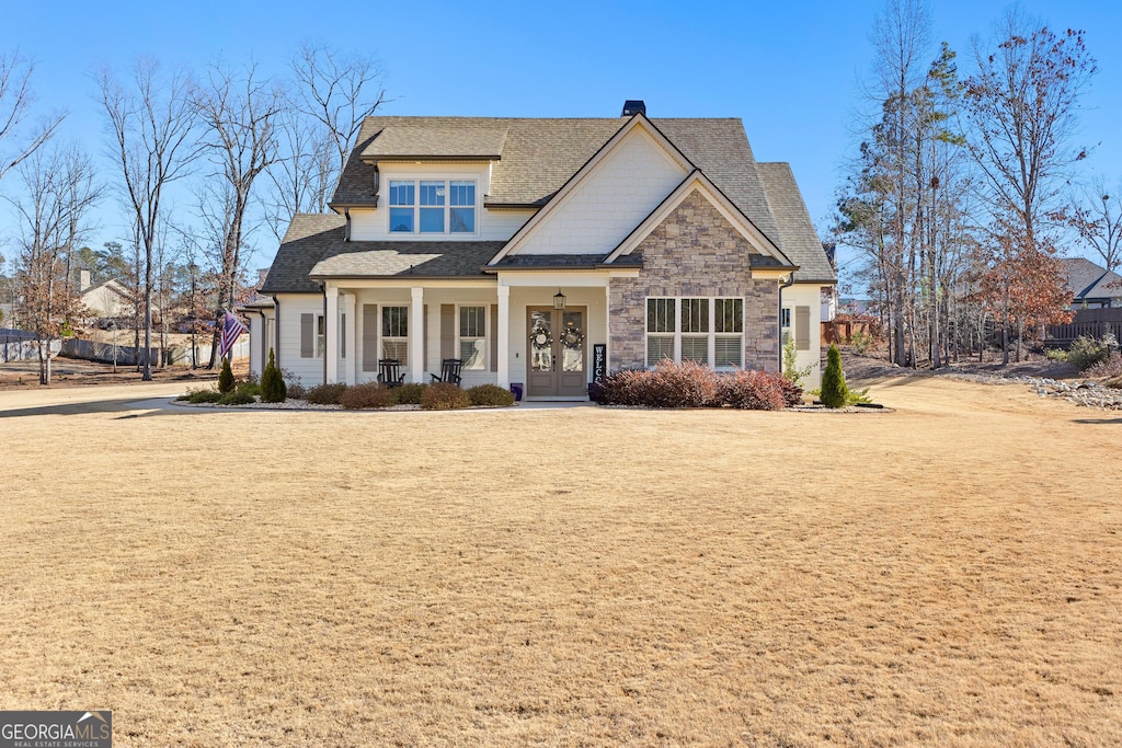 craftsman-style home with stone siding, roof with shingles, a front lawn, and french doors