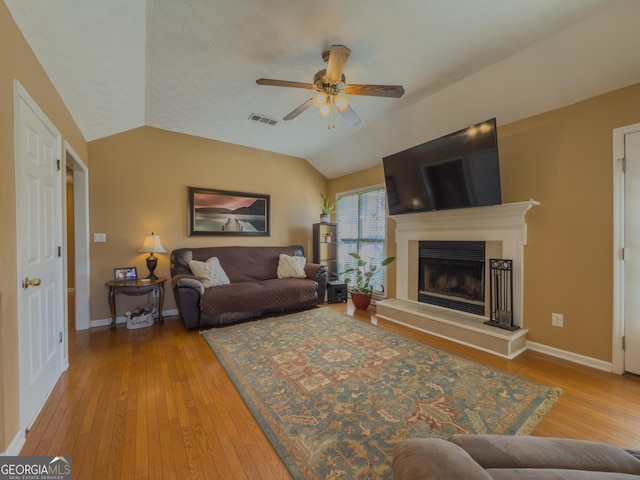 living room with vaulted ceiling, a fireplace with raised hearth, wood-type flooring, and visible vents