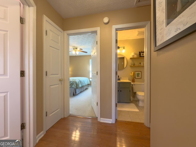 hall with baseboards, a sink, a textured ceiling, and hardwood / wood-style floors