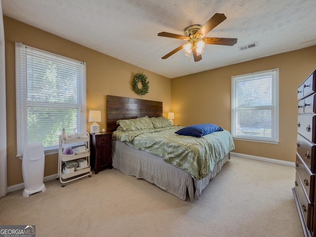 bedroom featuring baseboards, visible vents, a ceiling fan, light colored carpet, and a textured ceiling