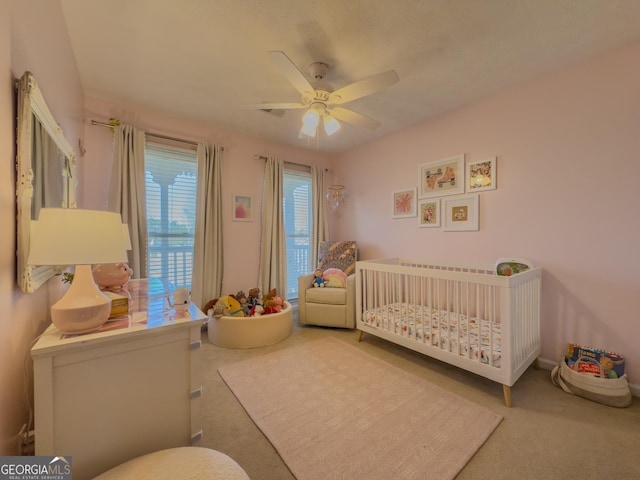 carpeted bedroom with a nursery area and a ceiling fan