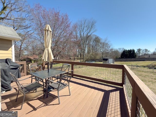 wooden deck with an outbuilding, a storage shed, area for grilling, fence, and outdoor dining space