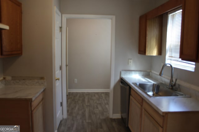 kitchen featuring baseboards, dishwasher, wood finished floors, light countertops, and a sink