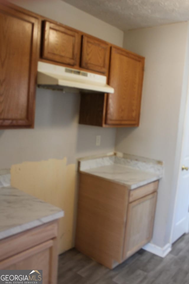 kitchen with under cabinet range hood, a textured ceiling, dark wood finished floors, and light countertops