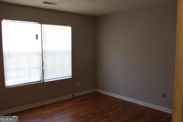 unfurnished room featuring dark wood-style floors, visible vents, and baseboards