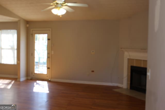 unfurnished living room with a tiled fireplace, wood finished floors, a ceiling fan, and baseboards