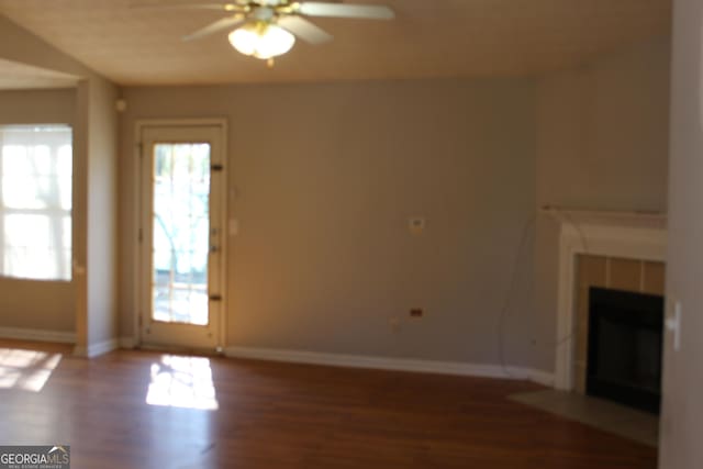 unfurnished living room featuring a tile fireplace, ceiling fan, baseboards, and wood finished floors