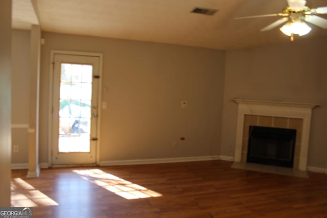 unfurnished living room with wood finished floors, plenty of natural light, a tile fireplace, and a ceiling fan