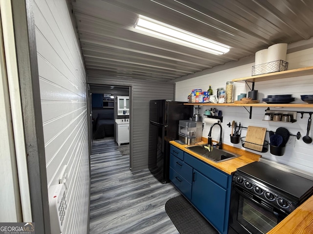 kitchen with butcher block counters, wood finished floors, blue cabinets, black appliances, and a sink